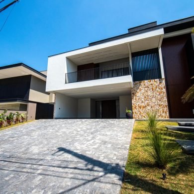 Fachada com revestimento de pedra natural anti-maresia, área externa com palmeira e jardim